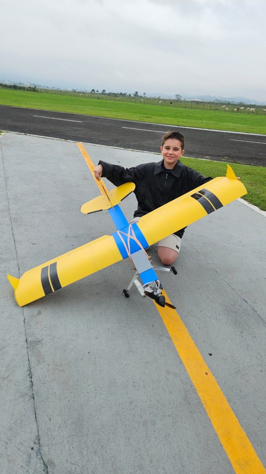 Thiago, 10 anos, ao lado do aeromodelo treinador na pista